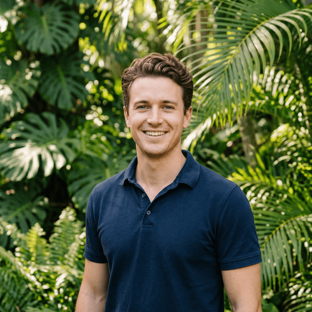 Profile photo of a smiling man in front of tropical foliage.